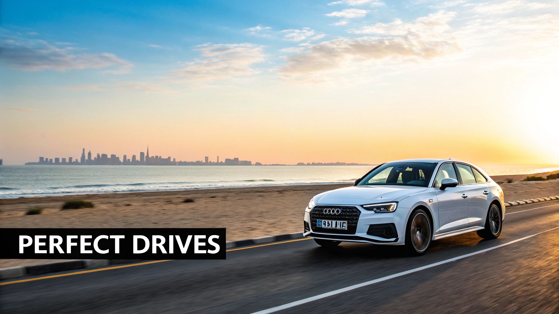 A white Audi car driving on a scenic coastal road at sunset with a city skyline.