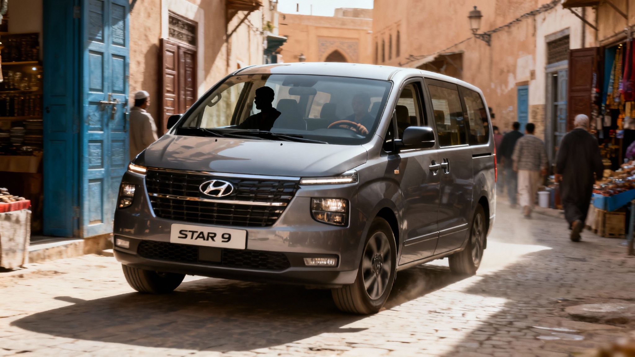Un van Hyundai gris roule sur une rue pavée animée dans une ville méditerranéenne ensoleillée.