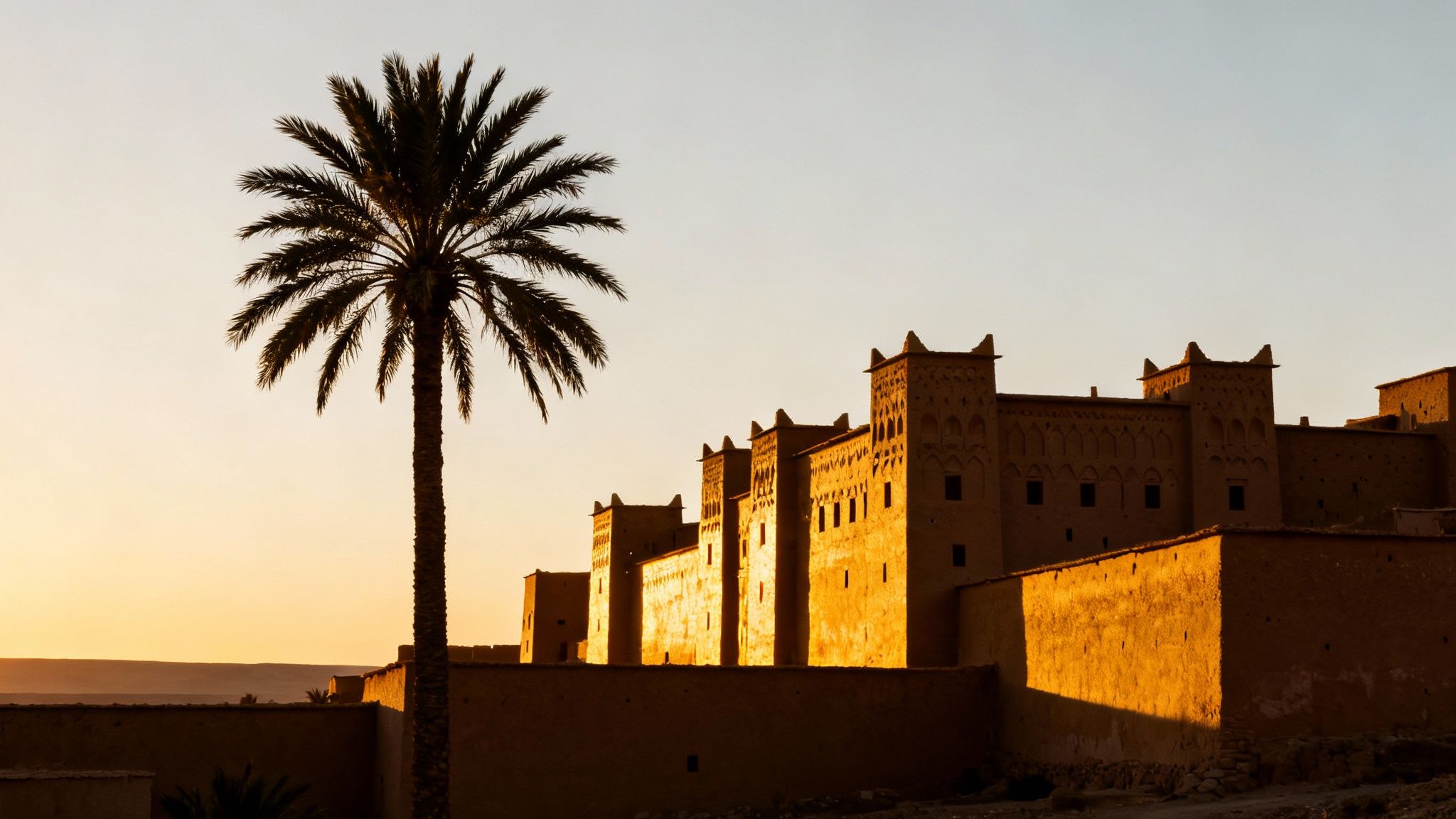 Kasbah traditionnelle marocaine en terre rouge au coucher du soleil avec palmier