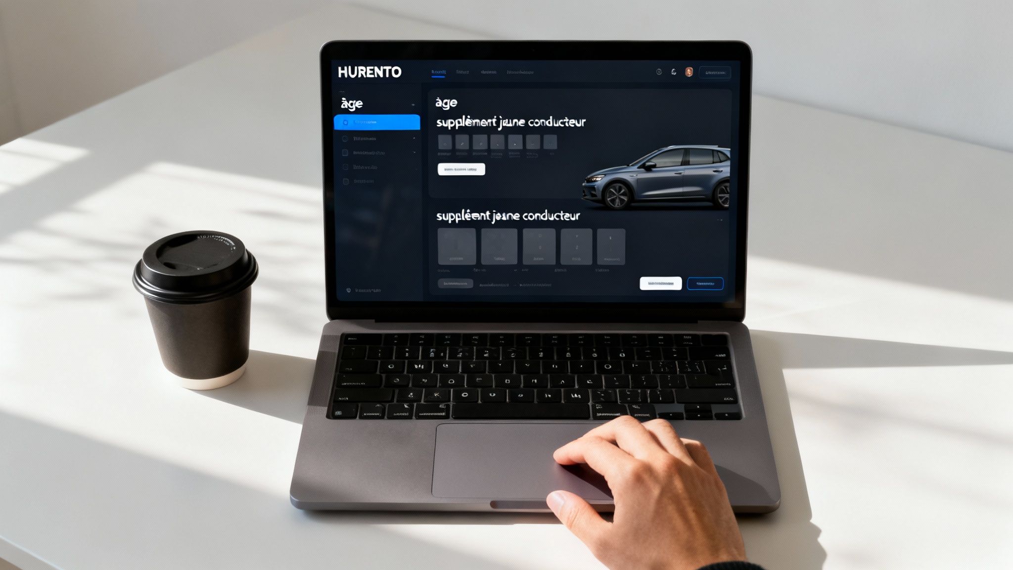 Utilisateur naviguant sur le site HURENTO de location de voiture pour jeunes conducteurs, avec une tasse de café.