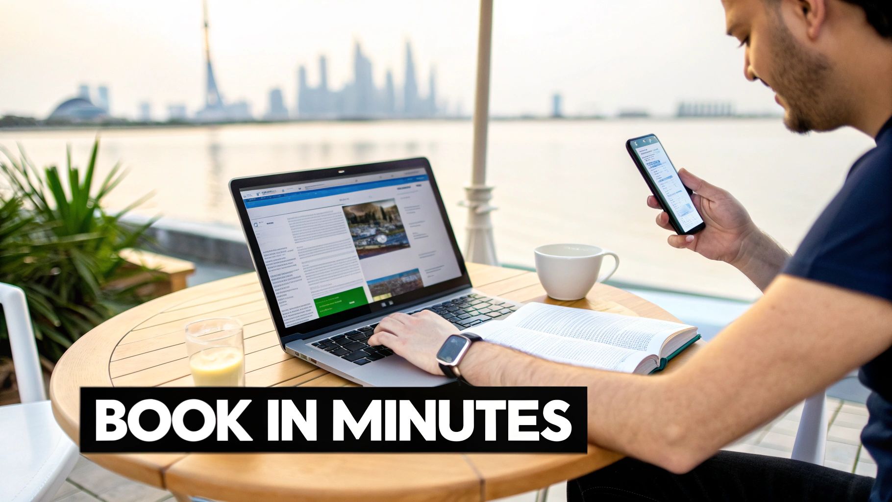 A man works on a laptop and smartphone outdoors with a city skyline in the background, making bookings.