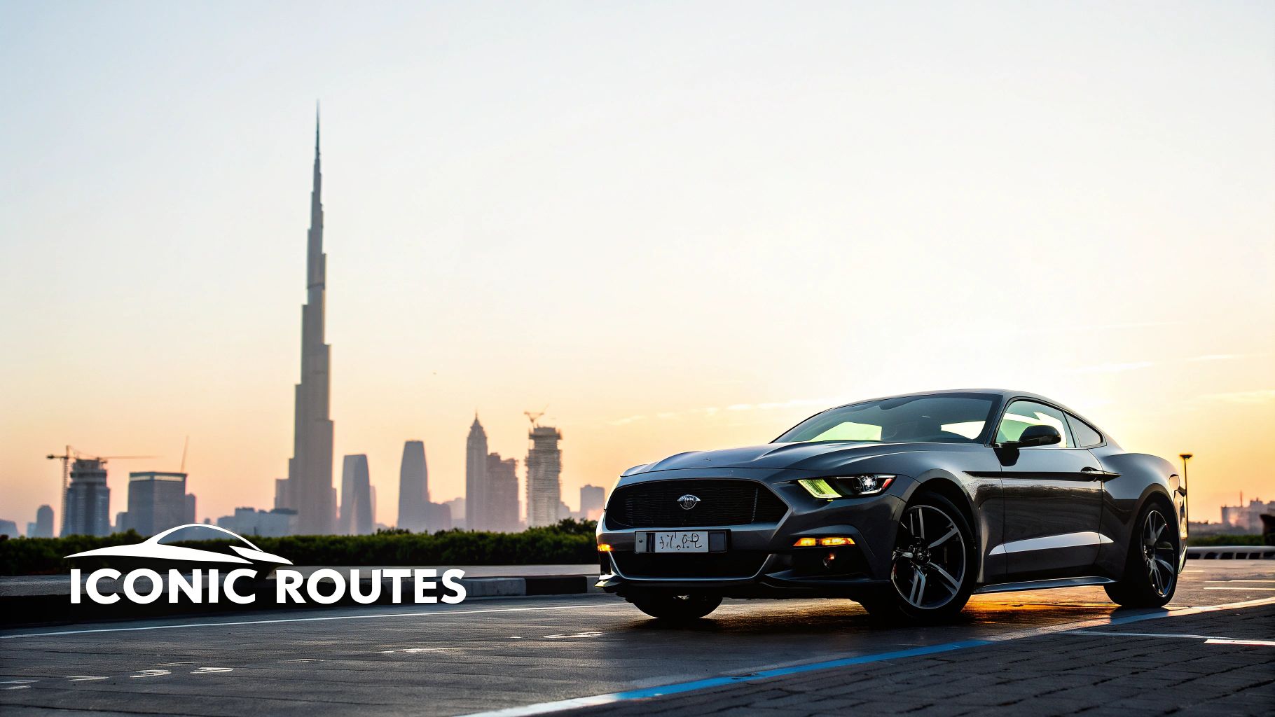 A sleek grey Ford Mustang car parked on a paved lot with Dubai's Burj Khalifa and skyline at sunset.