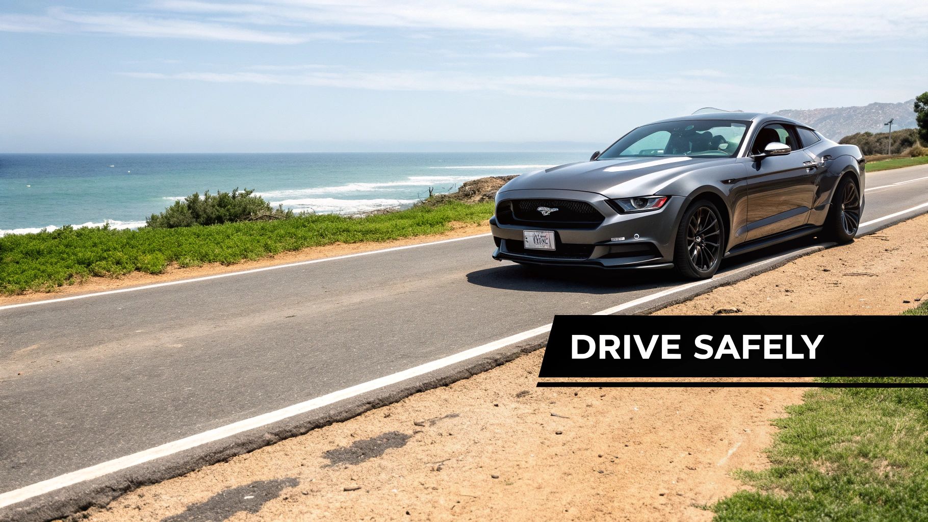 Your Guide to Mustang Dubai Rent 4 A sleek grey Ford Mustang parked on a scenic coastal road overlooking the ocean under a clear sky.