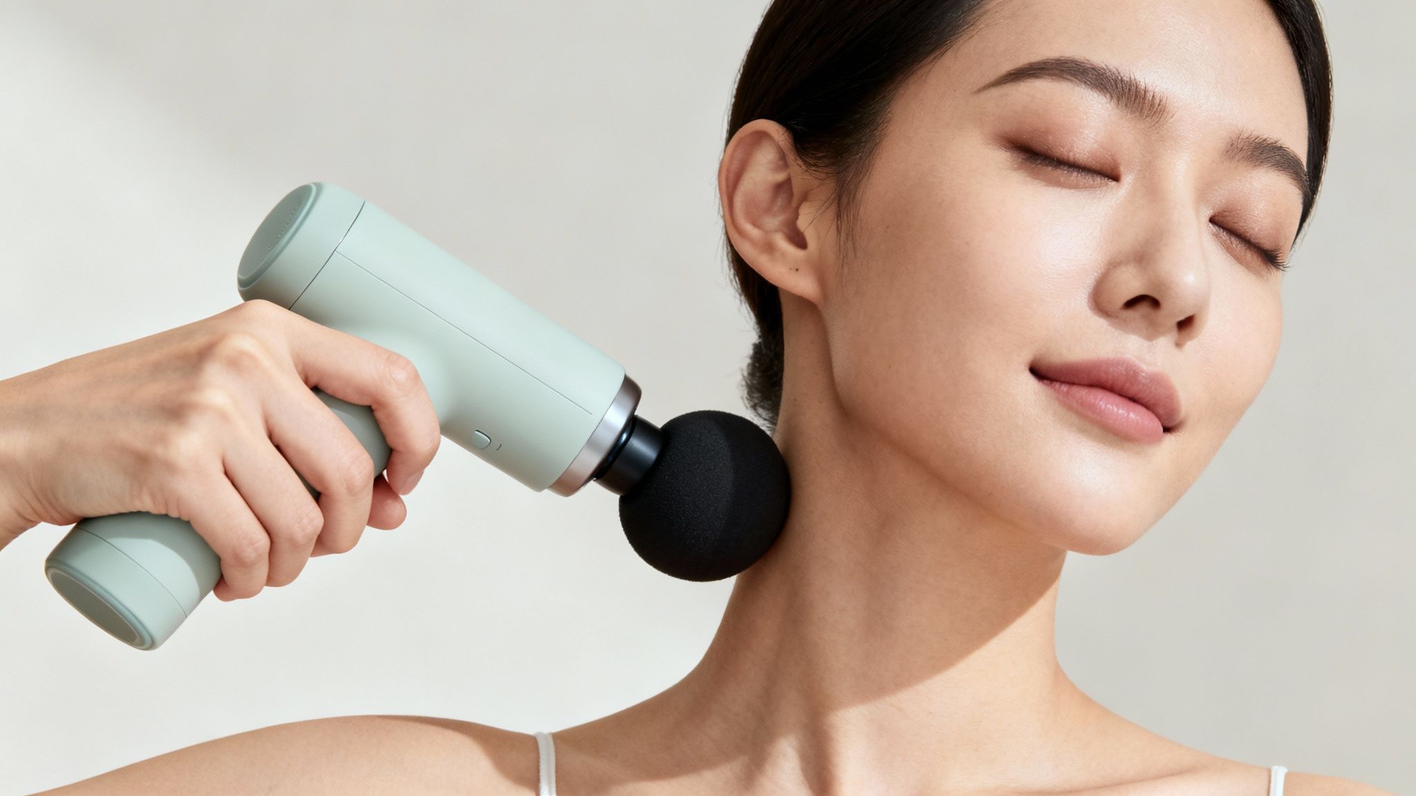 A person using a massage gun on their neck and shoulder area for pain relief.