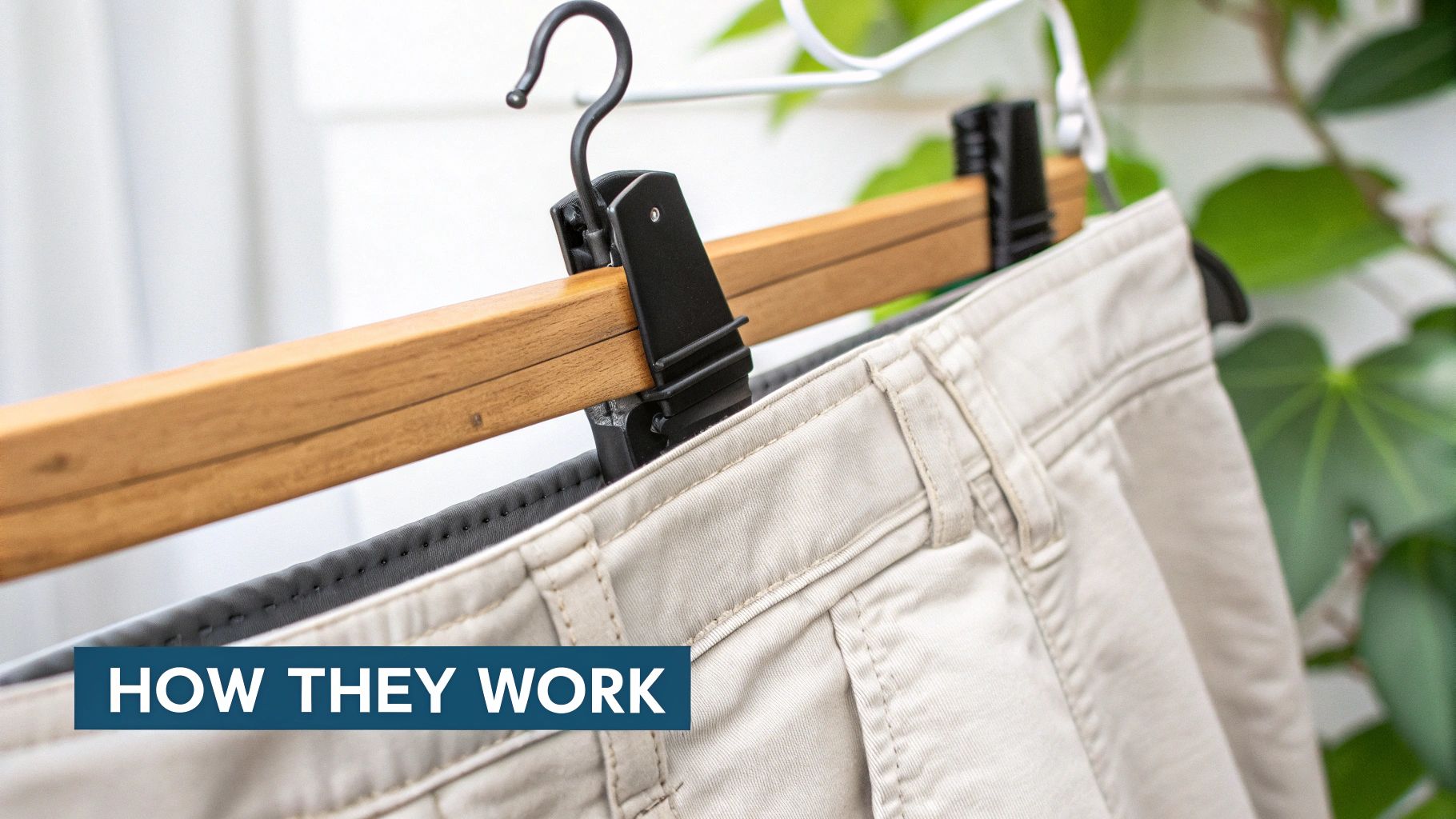 Close-up of beige pants hanging neatly on a wooden clamp hanger with black clips.