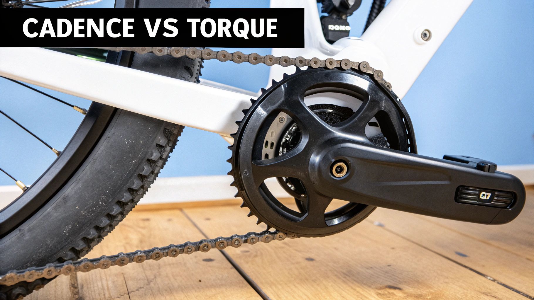 Close-up of a white electric bicycle's black crankset, chain, and tire with 'CADENCE VS TORQUE' text.