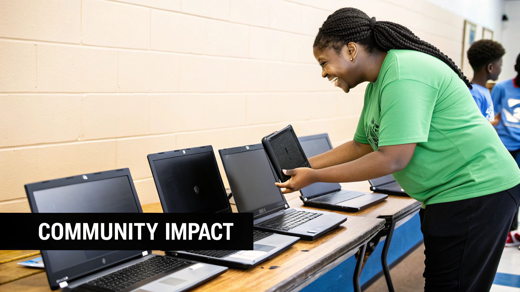 A smiling young Black woman sets up laptops and a tablet, embodying community impact.