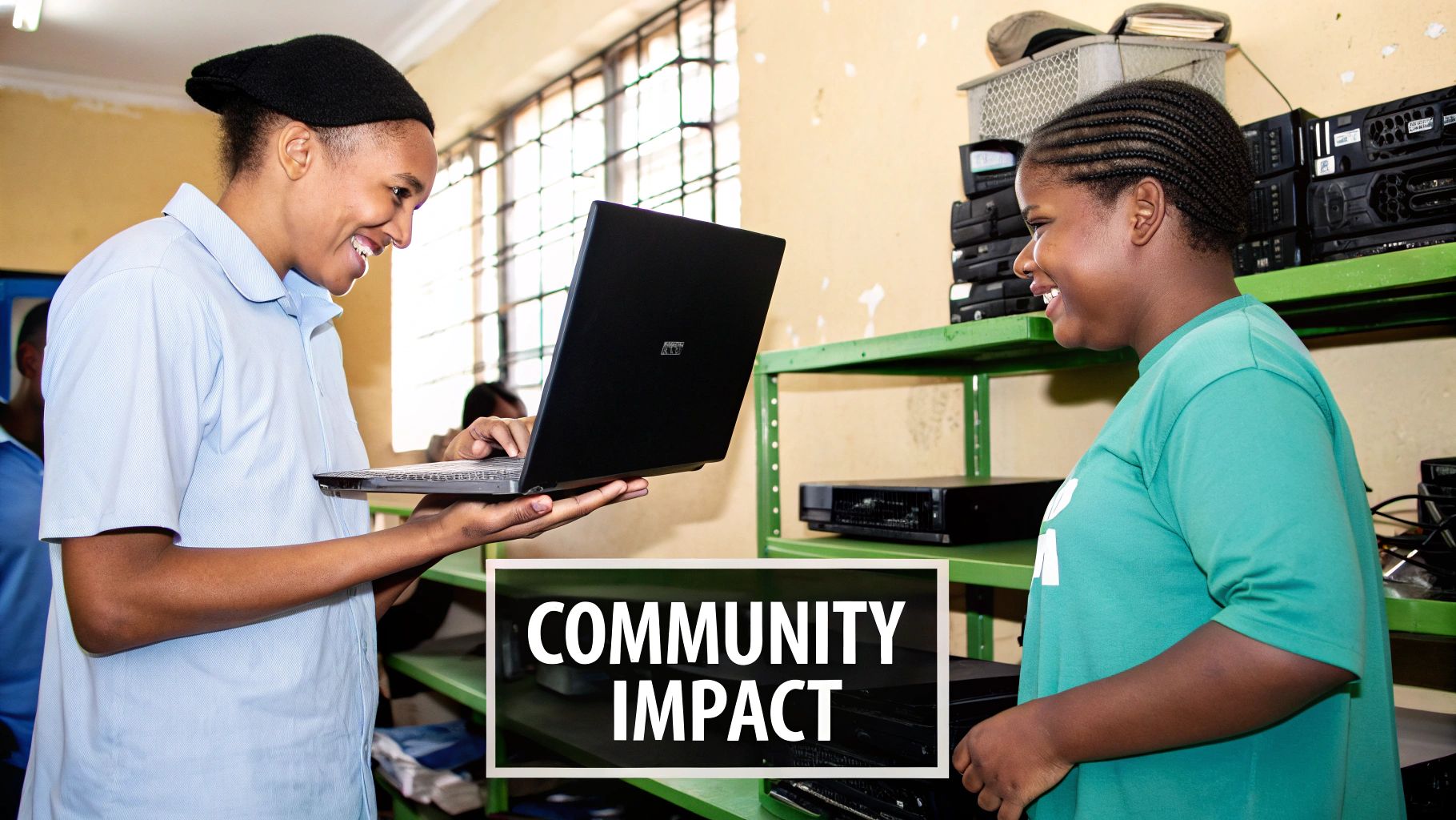 Two smiling young adults learn using a laptop amidst shelves of recycled electronics, demonstrating community impact.