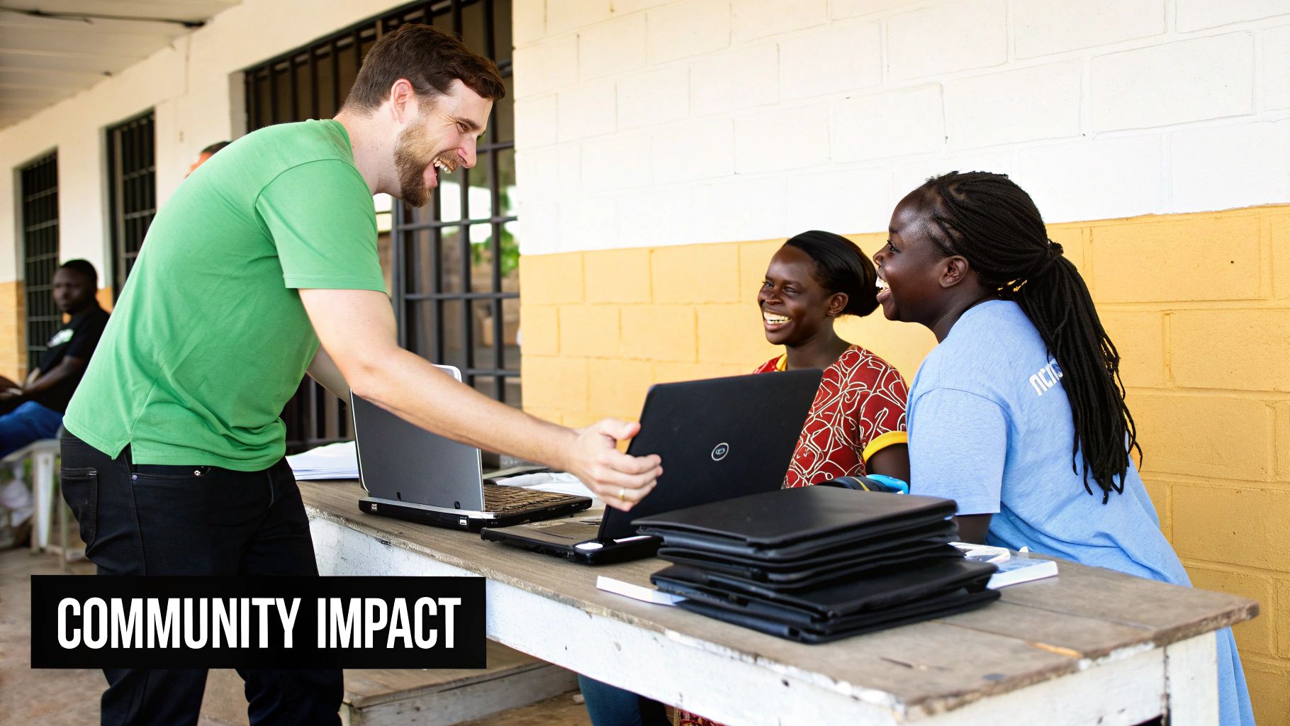 A smiling man shows a laptop to two engaged women at a table, highlighting community impact.