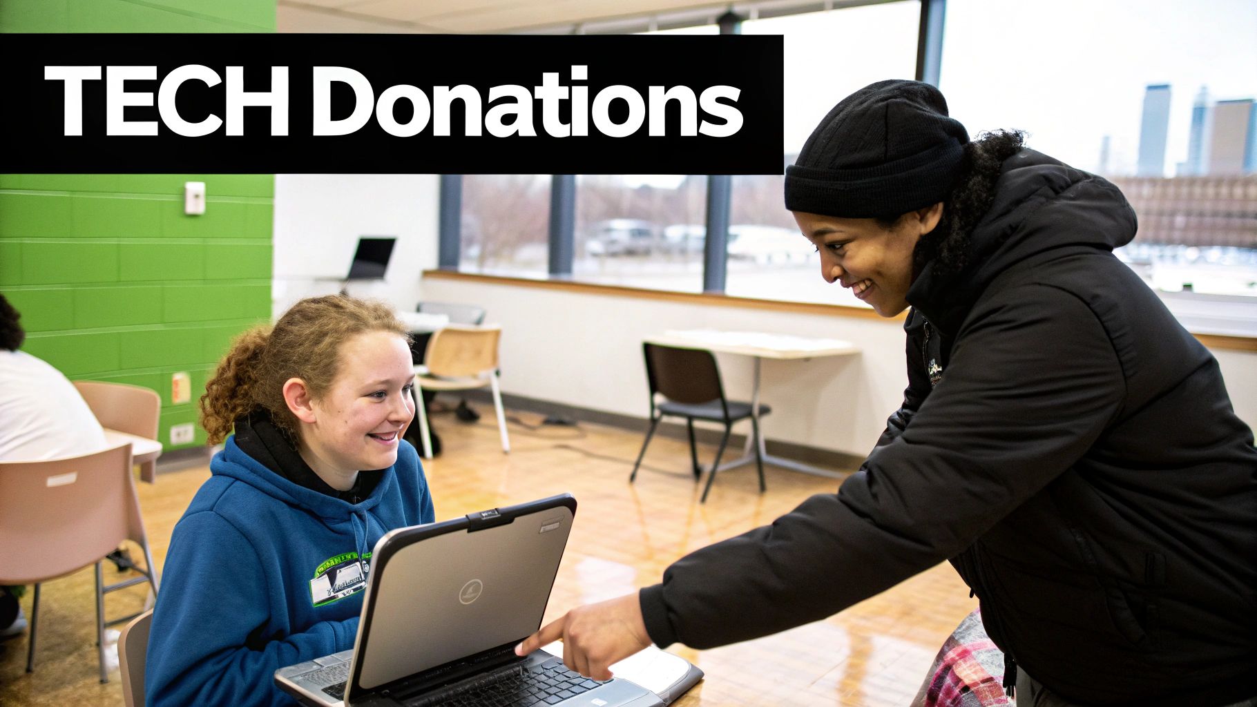Two smiling young people interact with a laptop in a classroom, celebrating tech donations.