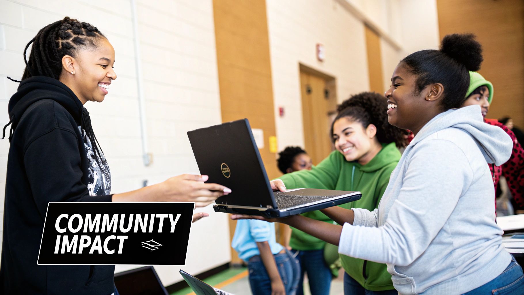 Smiling young women exchanging a laptop, indicating a community technology initiative.
