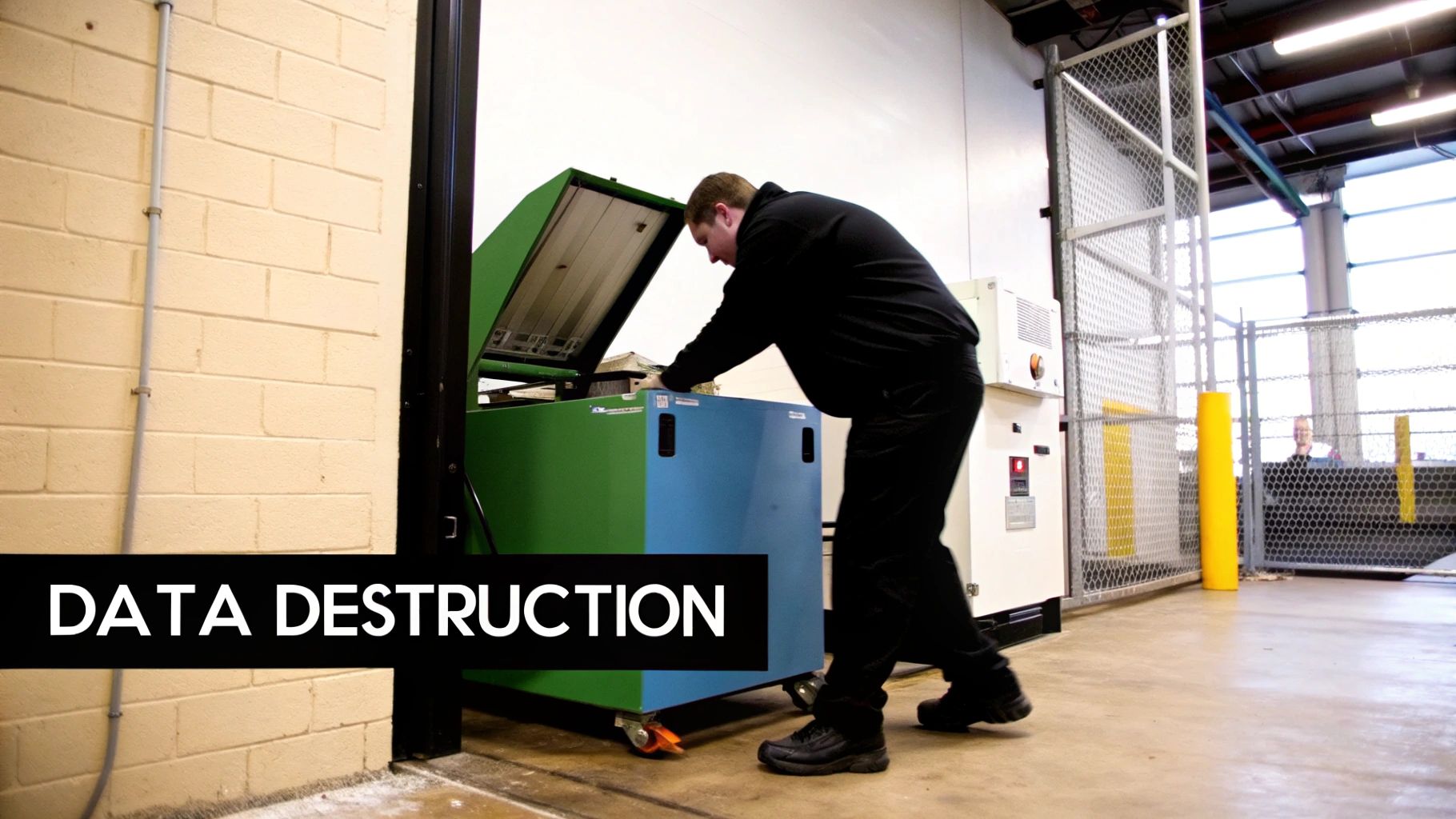A man in black loads hard drives into a green and blue data destruction machine.