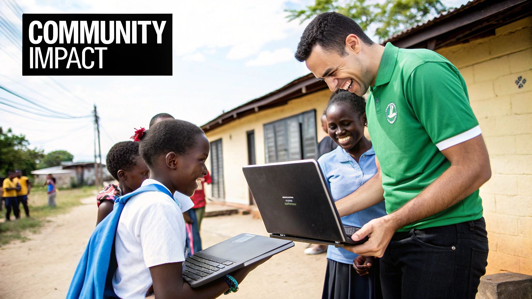 A smiling man in a green shirt helps joyful children learn with laptops in a rural community setting.