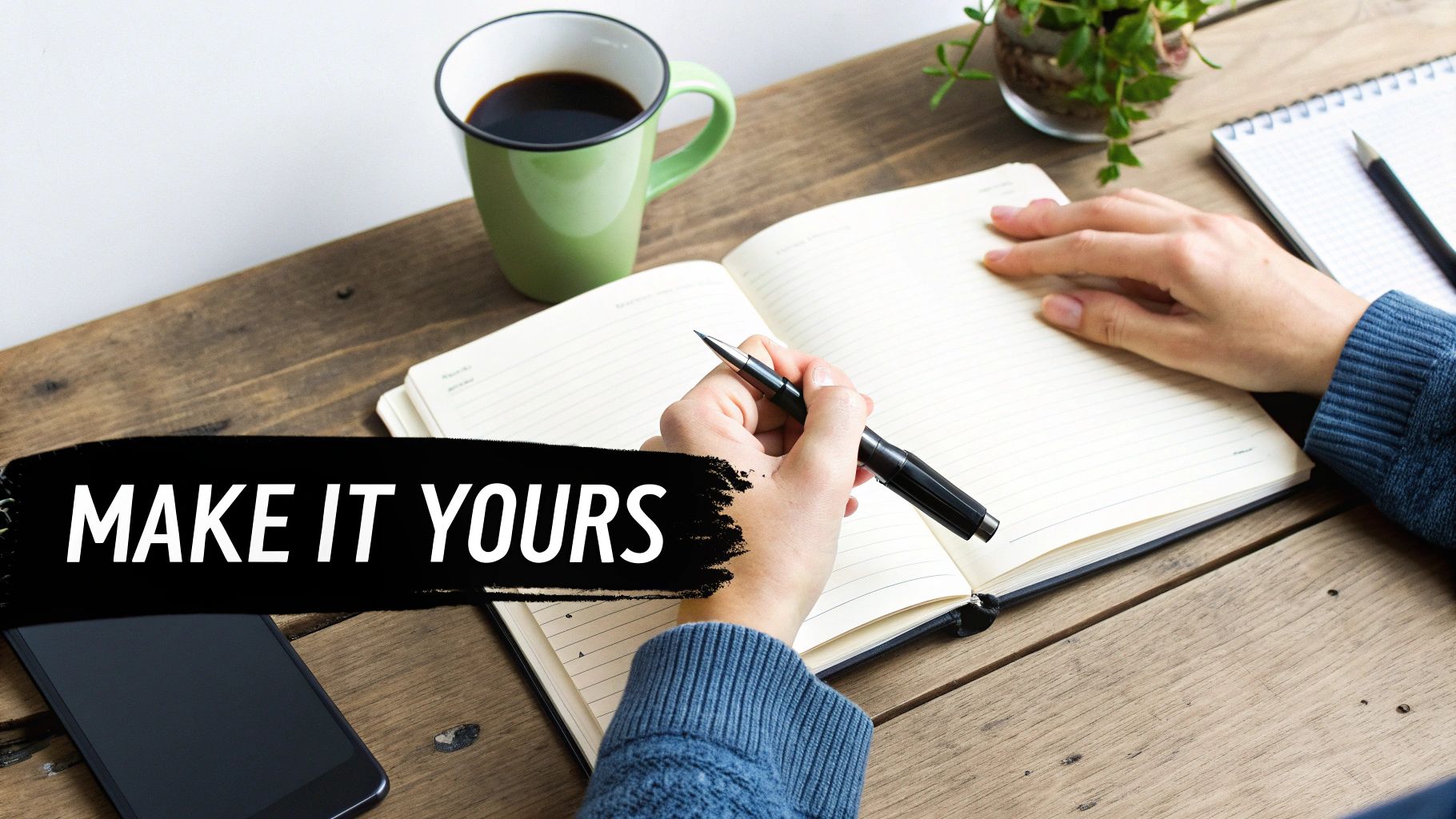 Close-up of hands writing in a journal with a pen on a rustic wooden desk with coffee and a phone.