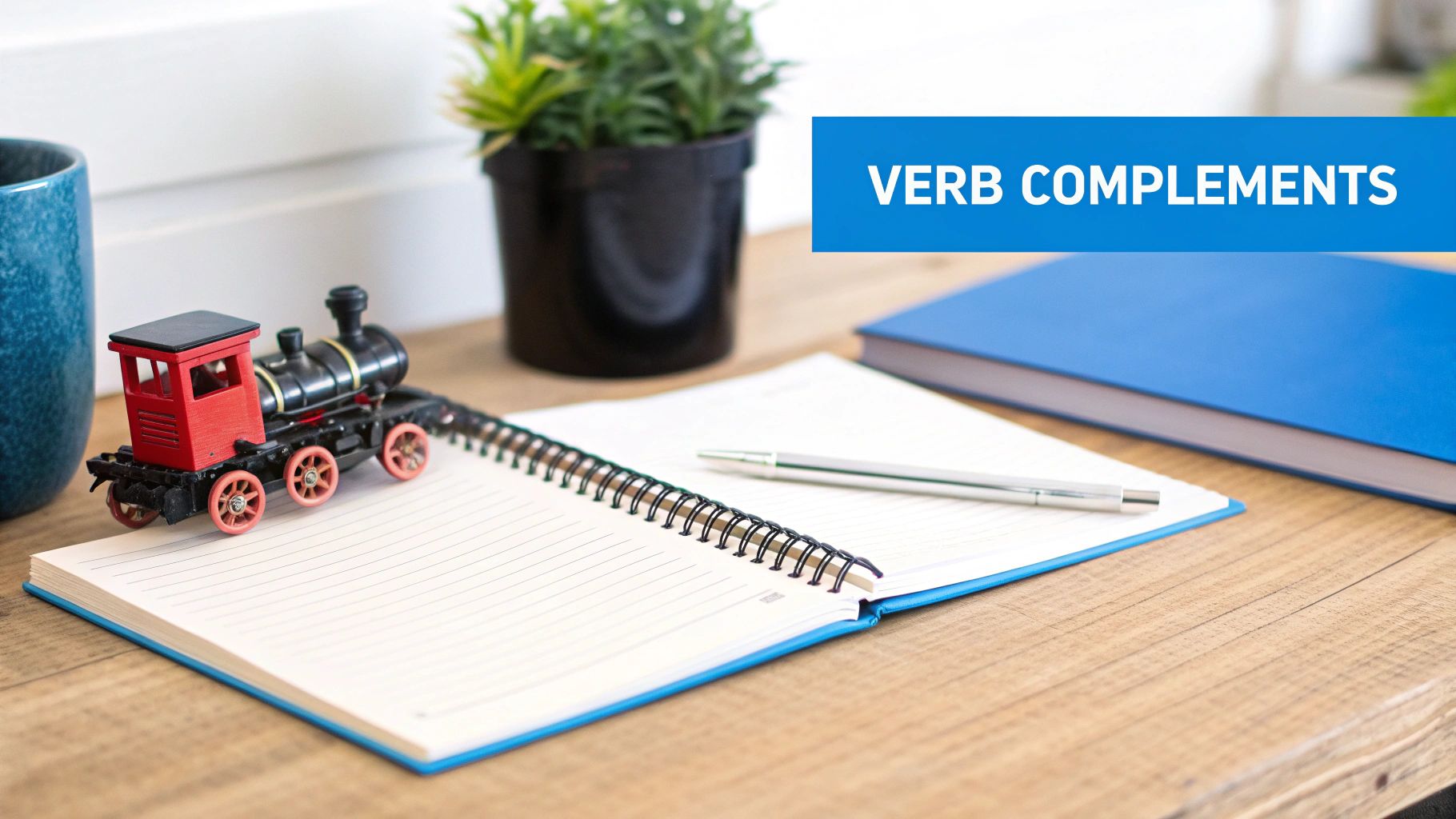 Desk workspace with toy train, notebook, pen and verb complements text overlay for grammar education