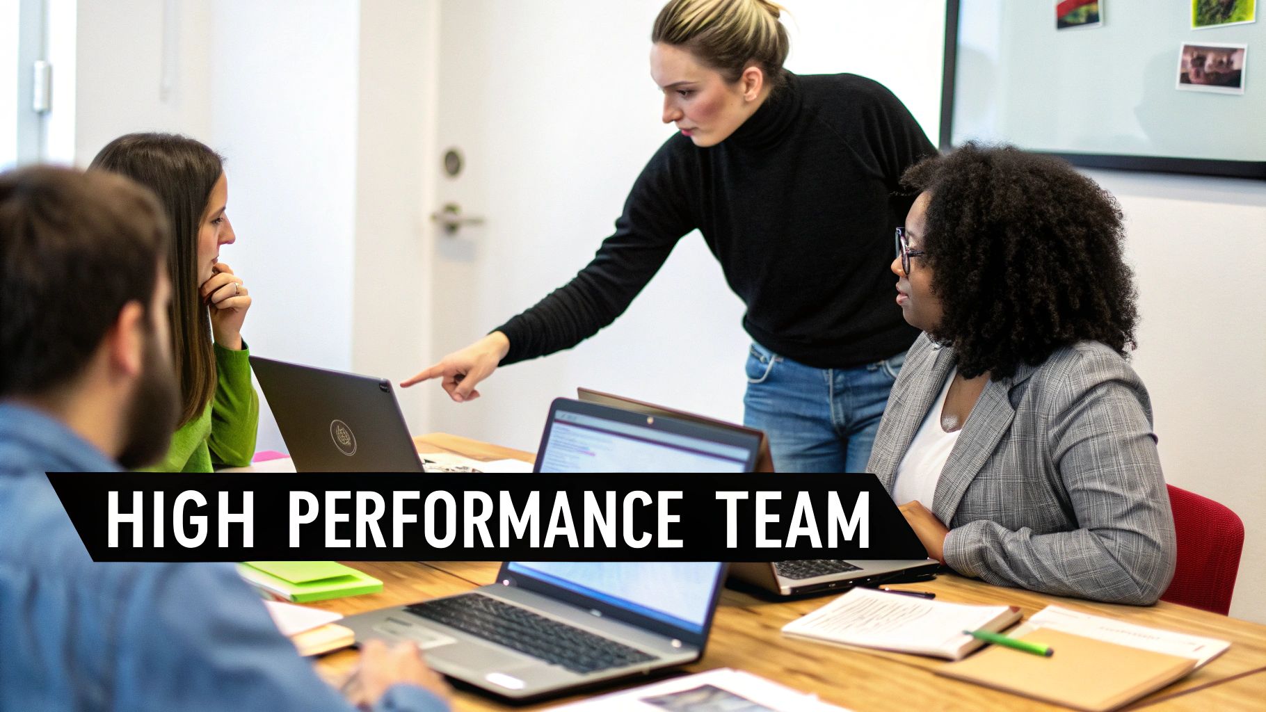 A diverse team collaborating around a table with laptops, one person pointing at a screen, embodying a high-performance team.