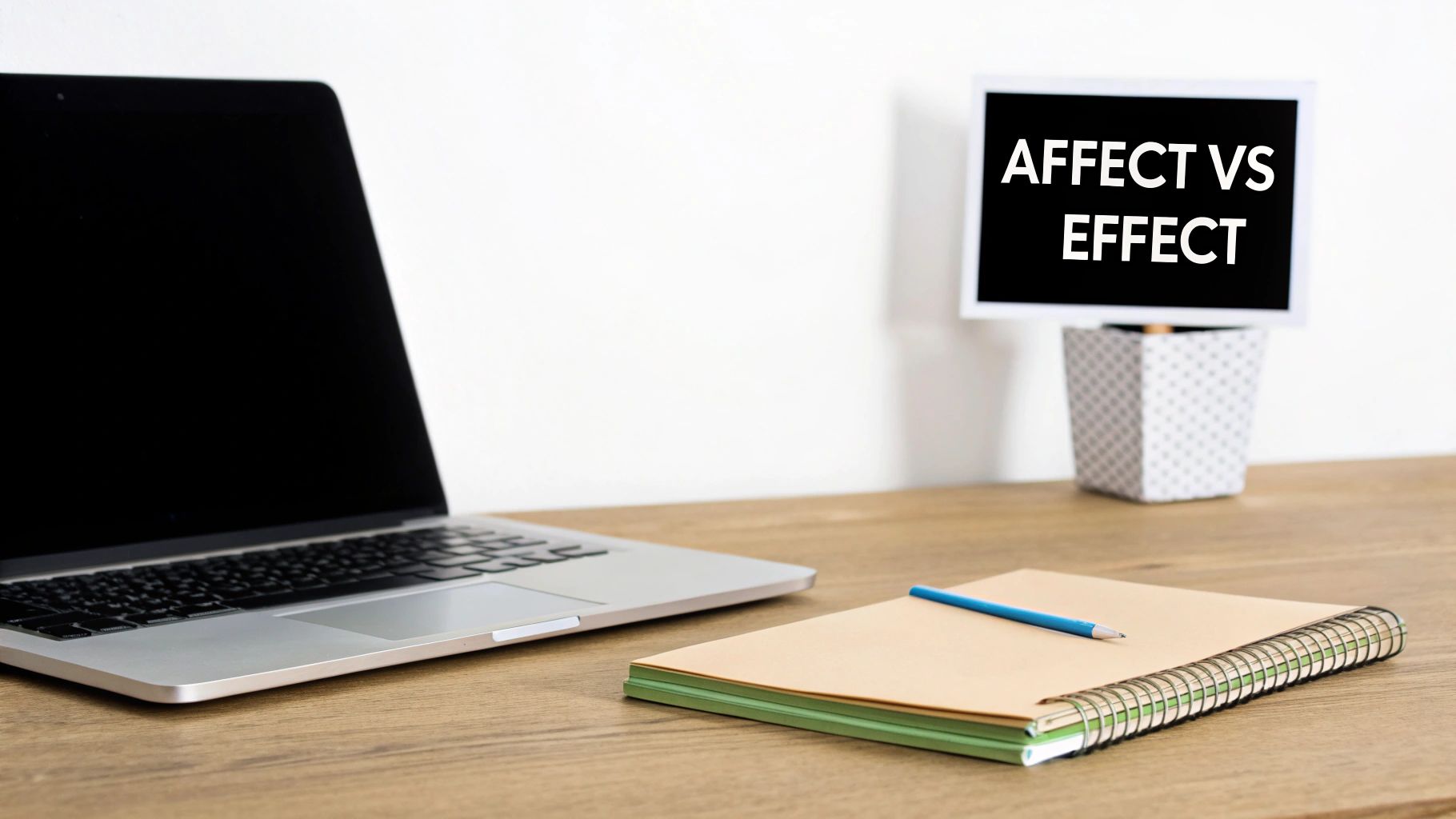 A desk setup with a laptop, a notebook, and a sign displaying 'AFFECT VS EFFECT' for grammar.