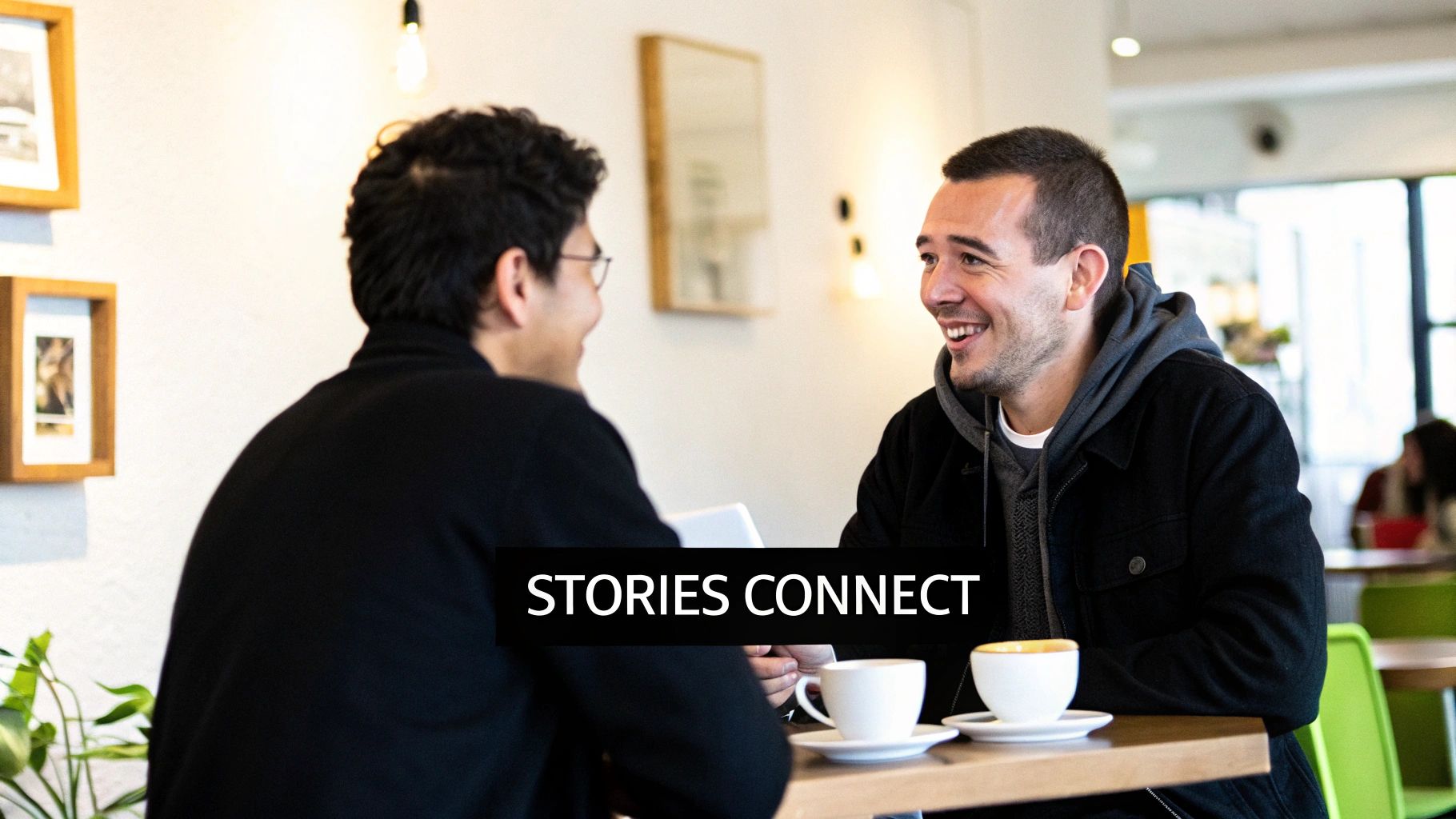 Two men smiling and talking over coffee in a cafe, suggesting a connection through stories.