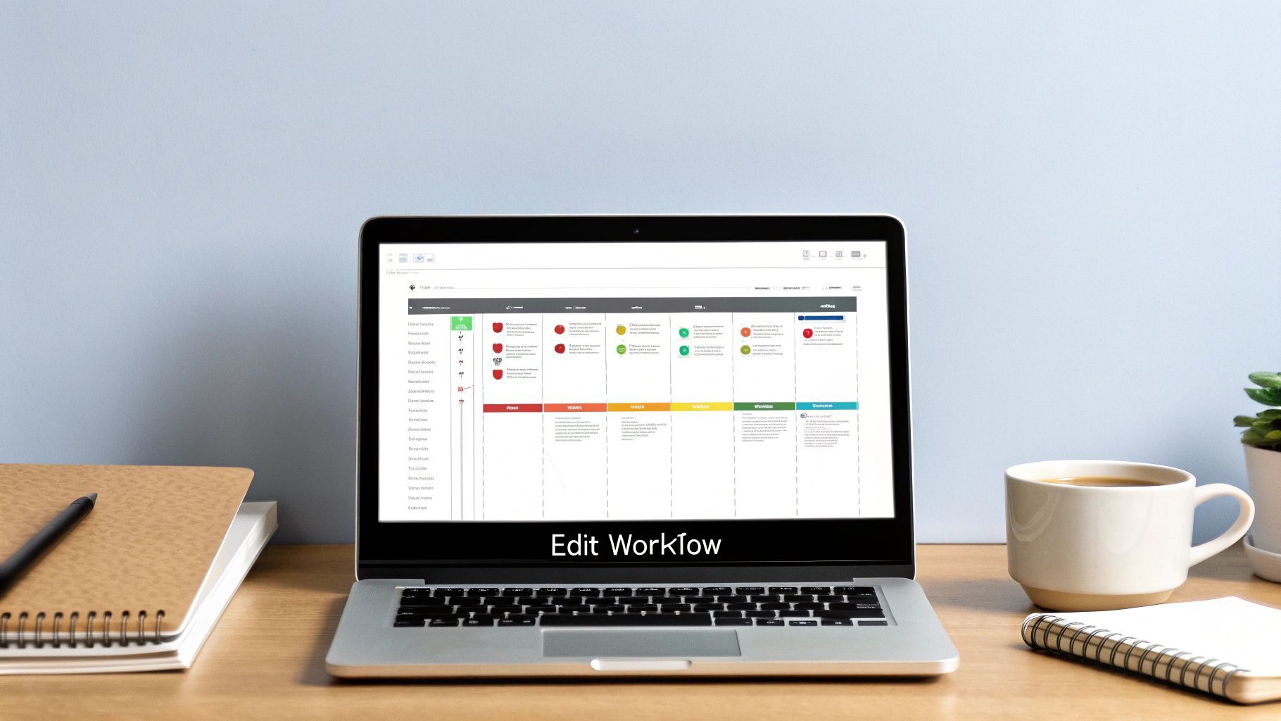 A laptop on a wooden desk displays a colorful workflow diagram, with a notebook and coffee mug.