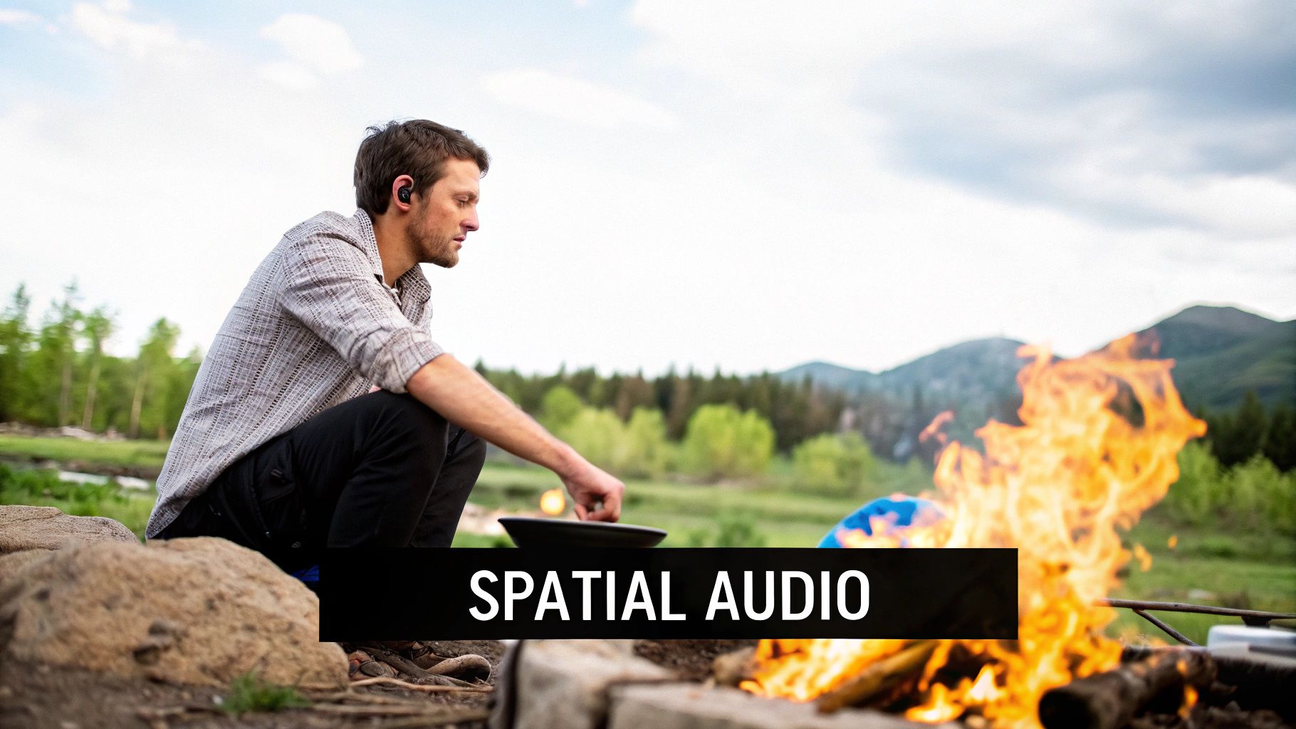 A man wearing wireless earbuds cooks over a campfire outdoors with 'SPATIAL AUDIO' text.