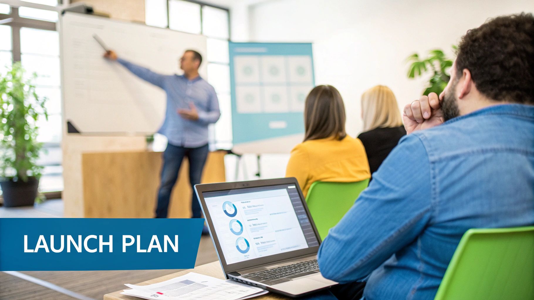 A man presents a launch plan on a whiteboard to a diverse group of colleagues in an office setting.