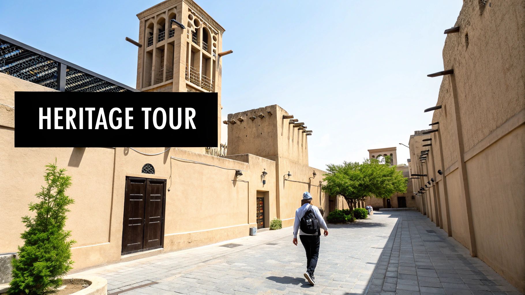 A person walks through a historic Middle Eastern street with traditional sand-colored buildings and a wind tower, labeled 'Heritage Tour'.