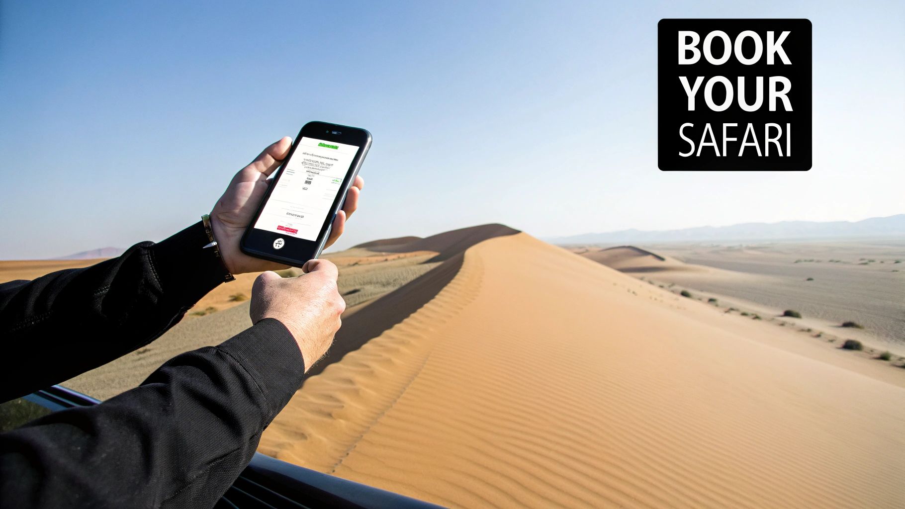 Hands holding a smartphone displaying a safari booking screen in a desert with sand dunes.
