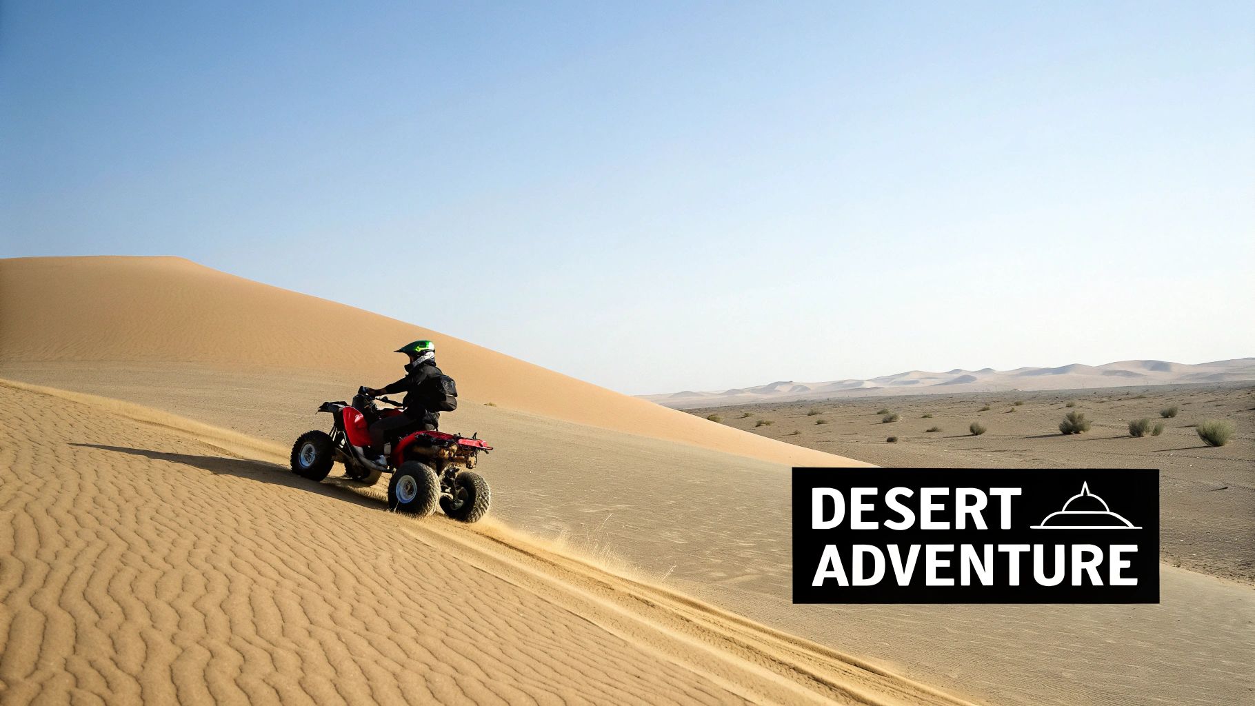 A person in a helmet riding a red quad bike down a large sand dune in a vast desert landscape.