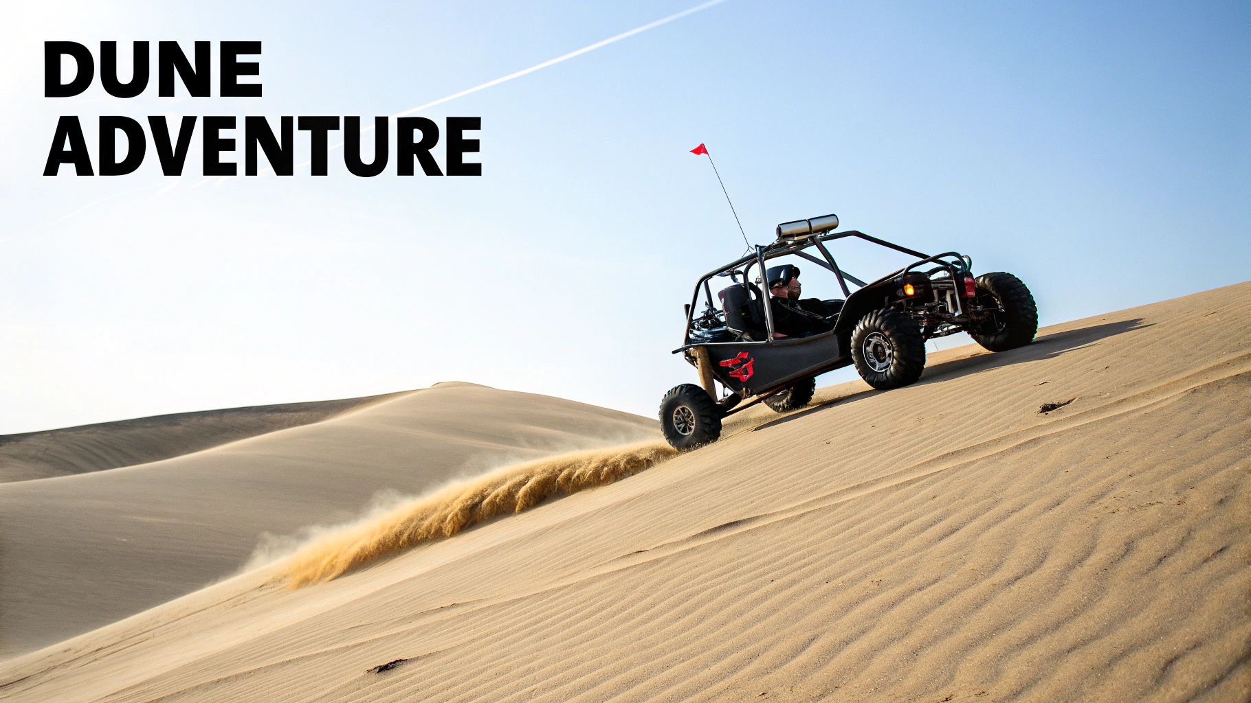 A black dune buggy driven by a person speeds up a large sand dune, kicking up sand, under a clear sky.