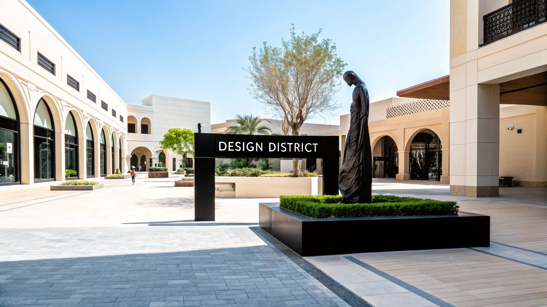 A sunny outdoor pedestrian area in Dubai's Design District with modern arched buildings and a dark sculpture.