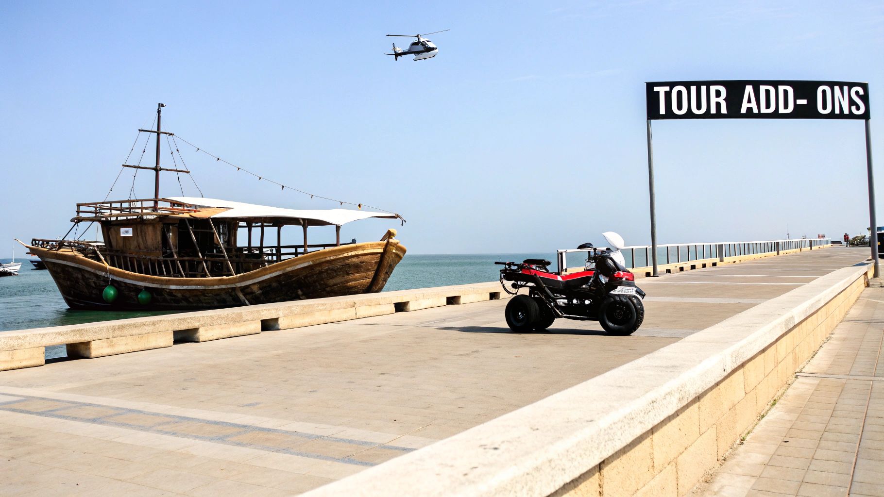 A traditional wooden boat docked beside a pier with an ATV, helicopter, and "TOUR ADD-ONS" sign under a clear sky.