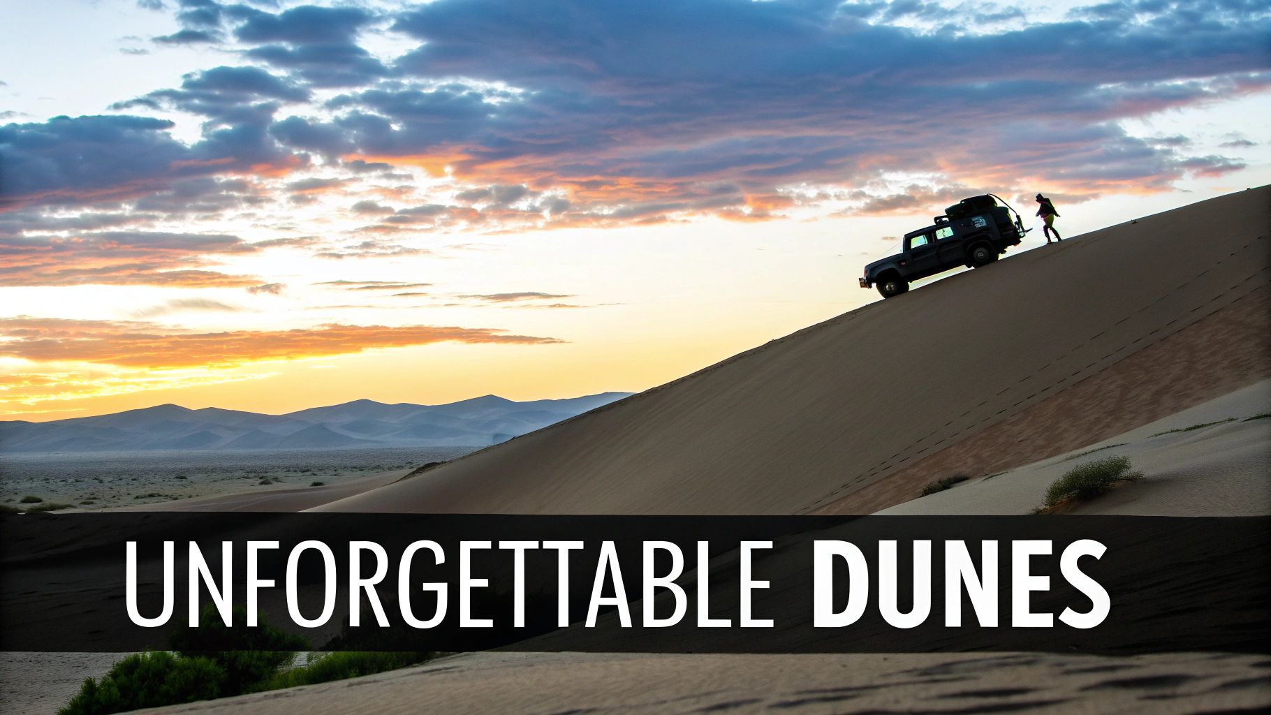 A dark SUV and a person ascend a tall sand dune at sunset in a vast desert landscape.