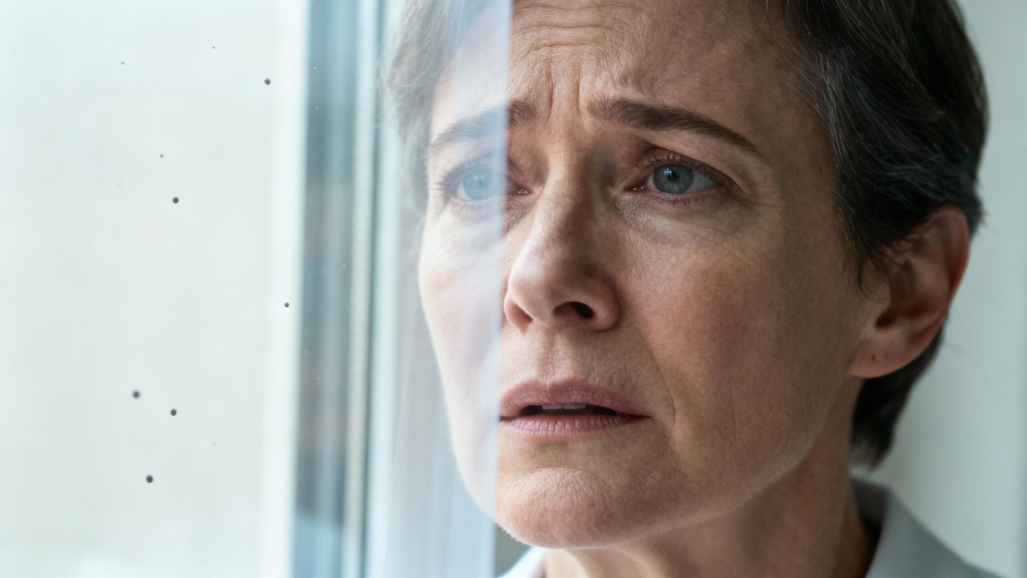 Mujer de mediana edad con expresión de preocupación, mirando a través de un cristal sucio o empañado.