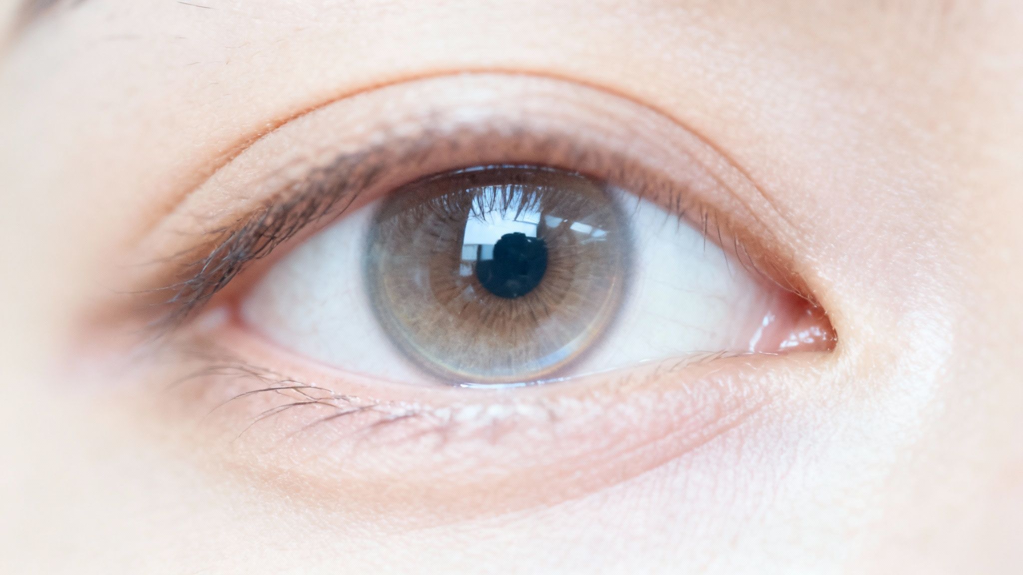 Primer plano de un ojo humano con iris marrón claro, pupila y reflejos sutiles.