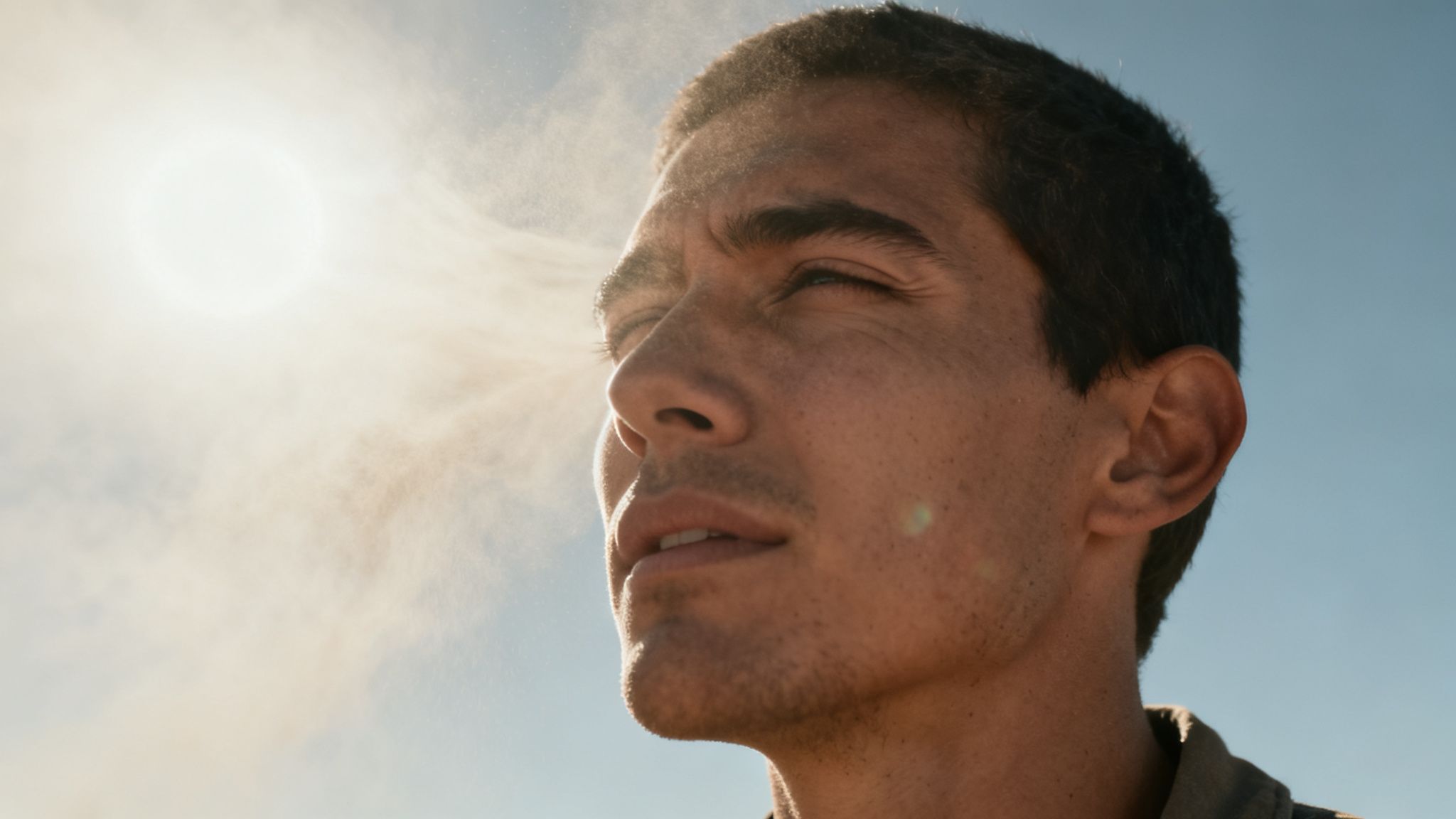 Primer plano de un hombre mirando hacia arriba, con el sol brillante y polvo en el aire.