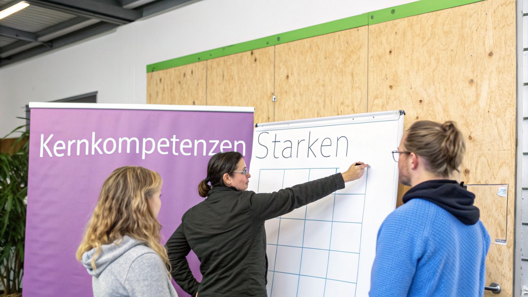 Eine Frau schreibt "Stärken" auf ein Whiteboard, umgeben von zwei Zuhörern bei einer Weiterbildung zu Kernkompetenzen.