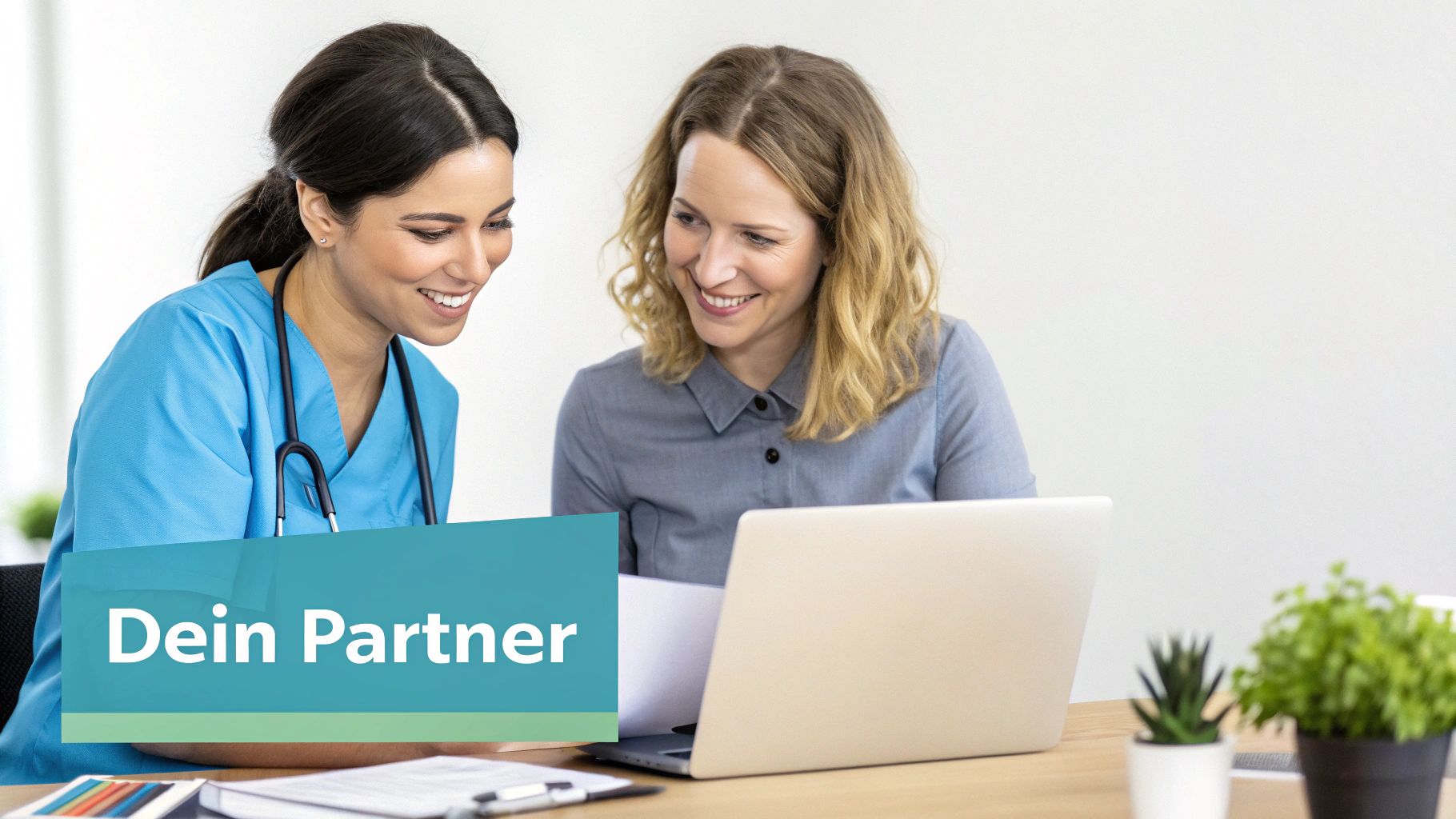 Zwei lächelnde Frauen, eine Pflegekraft und eine Geschäftsfrau, betrachten gemeinsam einen Laptop an einem Schreibtisch.