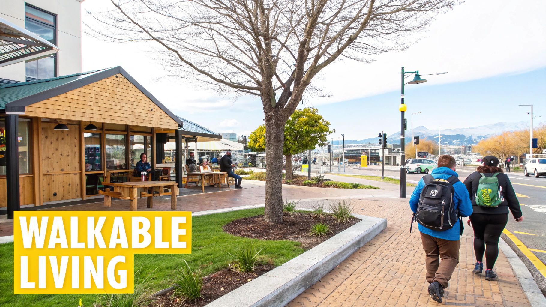 People walking on a pedestrian-friendly street with a cafe, trees, and distant snowy mountains.