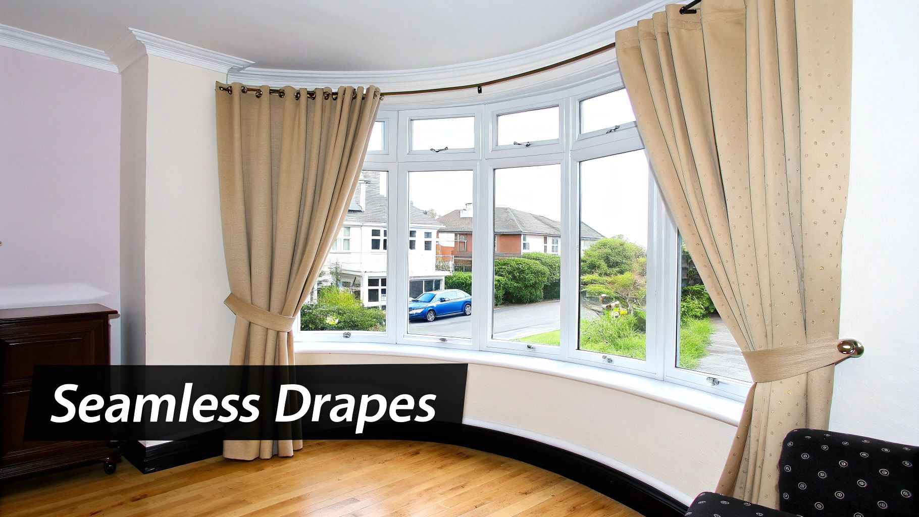 A room with a curved bay window featuring beige eyelet curtains tied back, showcasing houses and trees outside.