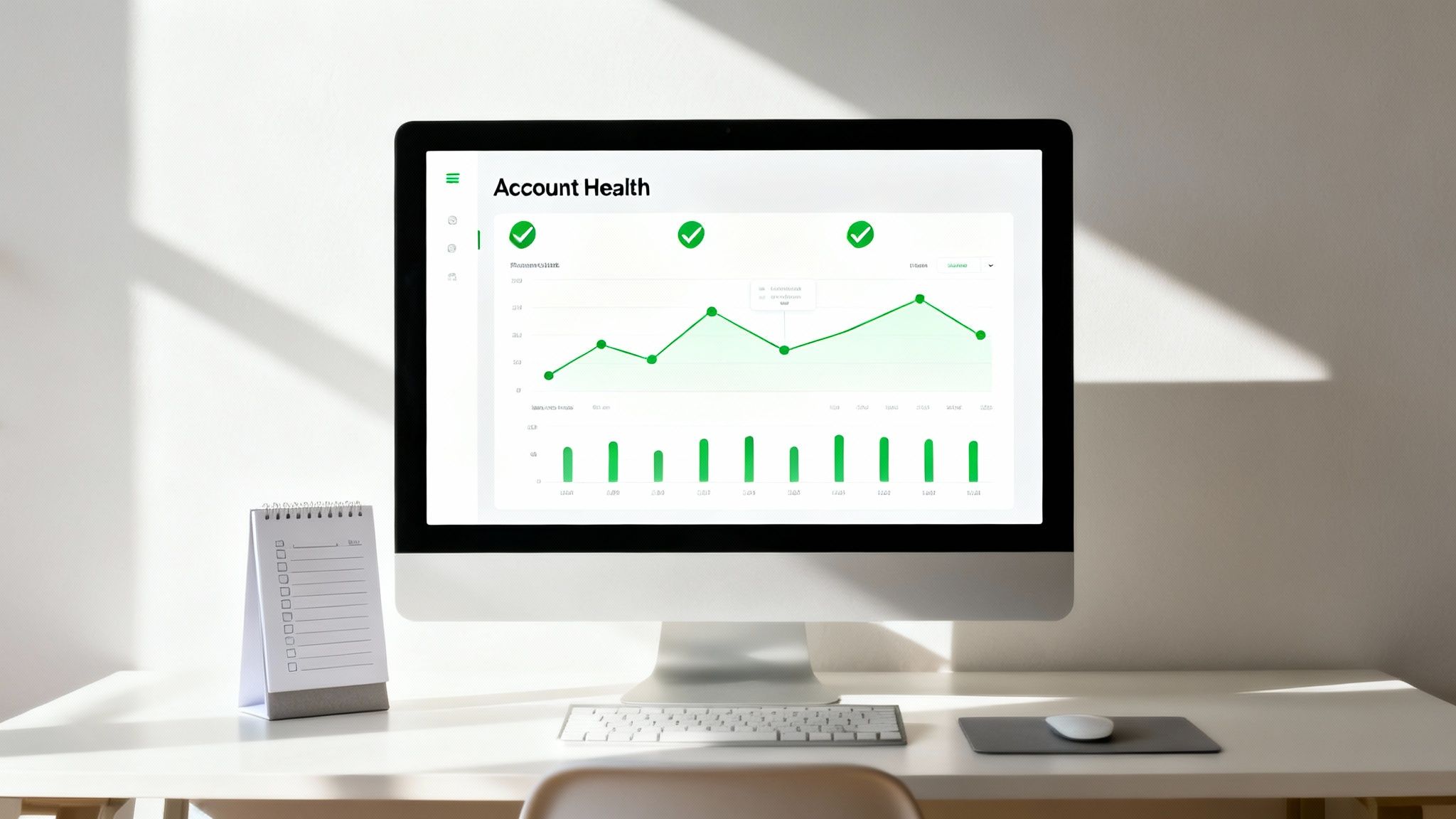 A minimalist white desk with a computer displaying an 'Account Health' dashboard and a notepad.