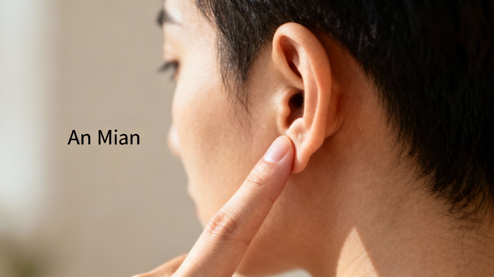 A person's finger gently presses the An Mian acupressure point located behind their earlobe.