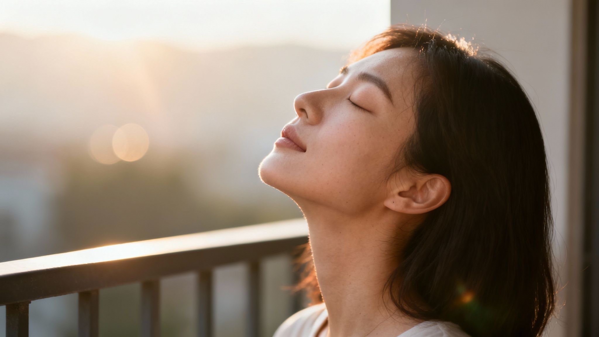 Eine junge Frau genießt entspannt die warme Sonne auf einem Balkon während des Sonnenuntergangs.