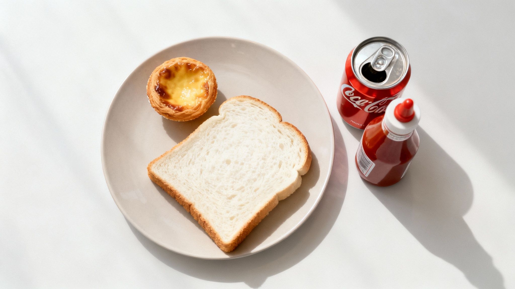 Un piatto con pane bianco e tortine alla crema, accanto una lattina di Coca-Cola aperta e una bottiglia di salsa rossa.