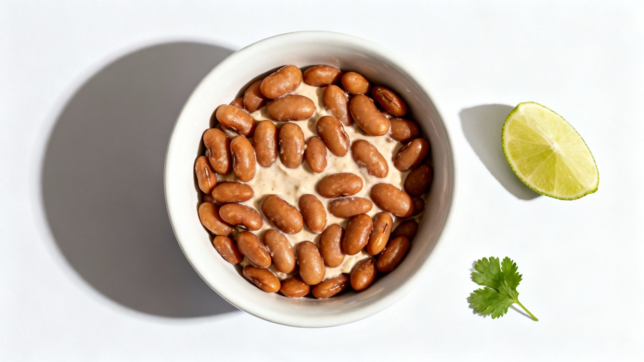 Overhead shot of a white bowl filled with pinto beans on a creamy sauce, garnished with a lime and cilantro.