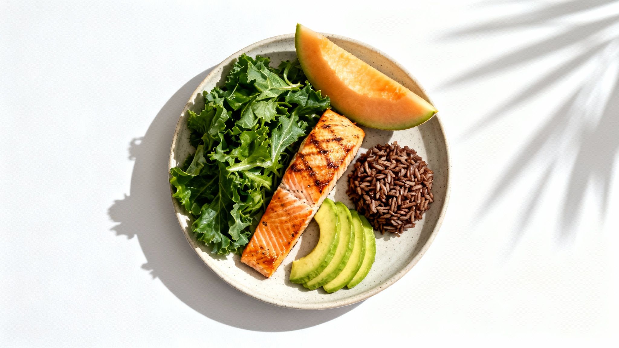 Healthy meal featuring grilled salmon, fresh kale, brown rice, avocado, and melon.