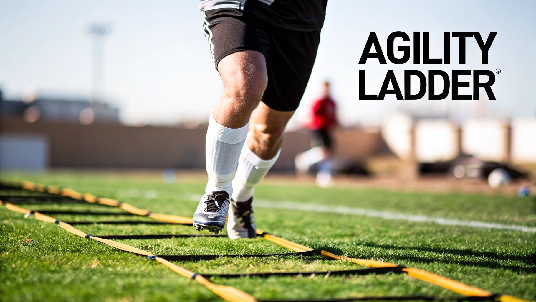A footballer performing a fast-footwork drill using a ladder for soccer laid out on the grass.