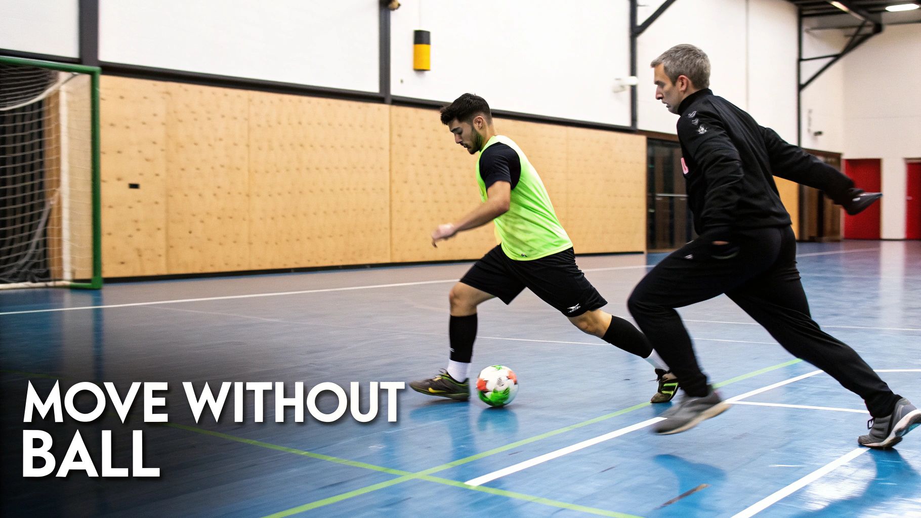 Two men practice futsal on an indoor court, one dribbling the ball, the other running alongside.
