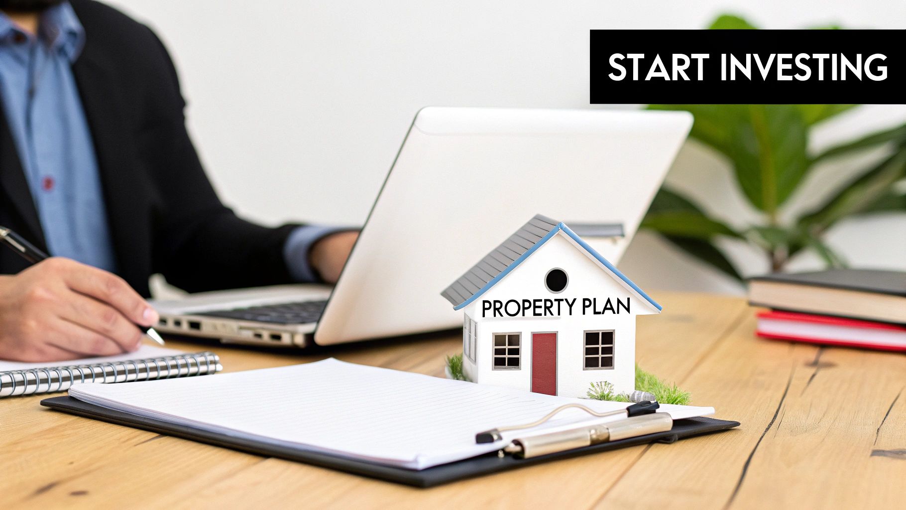 A person writing on a notepad and using a laptop, with a "PROPERTY PLAN" miniature house model.