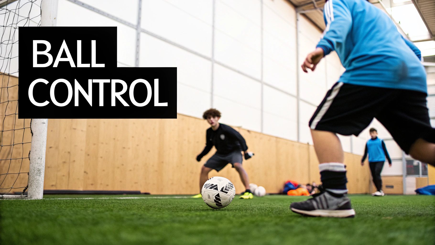 Young players practice ball control on an indoor football pitch with a goal.