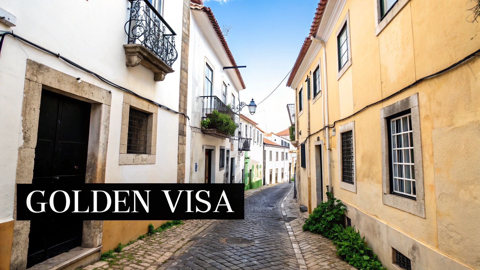 A charming, narrow cobblestone street winds through historic white and yellow buildings under a blue sky.